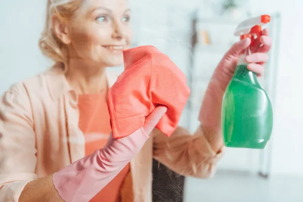 Donna anziana spensierata in guanti di gomma rosa finestra di pulizia — Foto stock