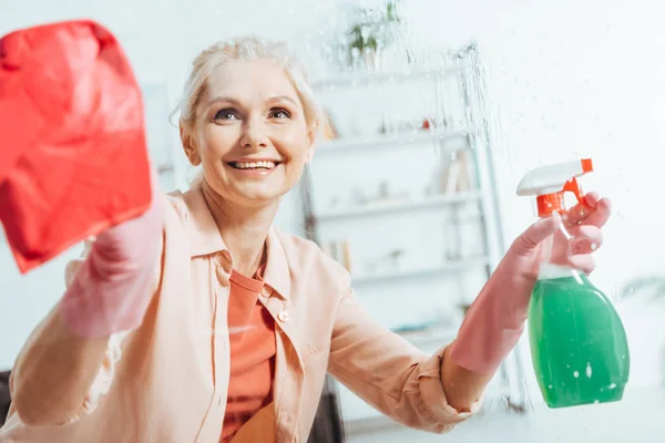 Blissful senior woman in rubber gloves cleaning window — Stock Photo