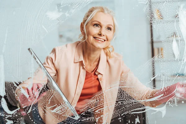 Усміхнена жінка прибирає вікно зі скляним склоочисником — стокове фото
