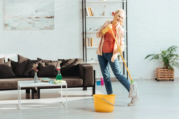 Riendo mujer mayor bailando mientras limpia piso con fregona - foto de stock