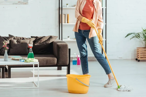 Обрізаний вид жінки в джинсах прибирання підлоги з мопедом — стокове фото