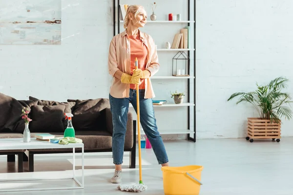 Dreamy senior woman posing with mop and cleaning supplies — Stock Photo