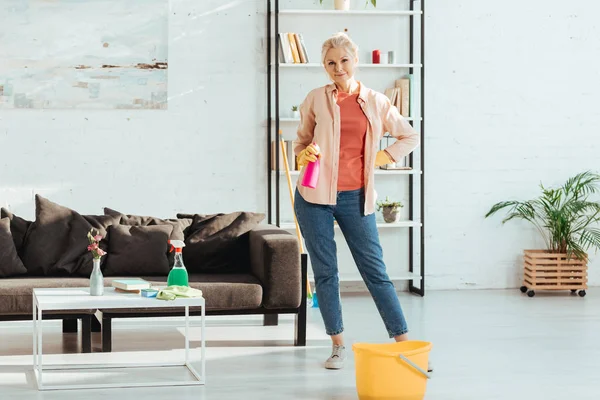 Agréable femme âgée posant avec des fournitures de nettoyage — Photo de stock