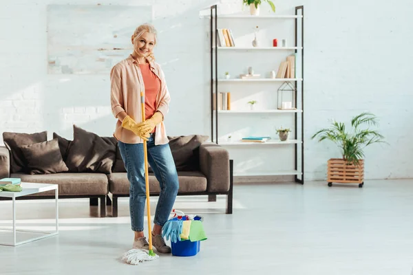 Glad senior woman with mop and bucket posing in living room — Stock Photo