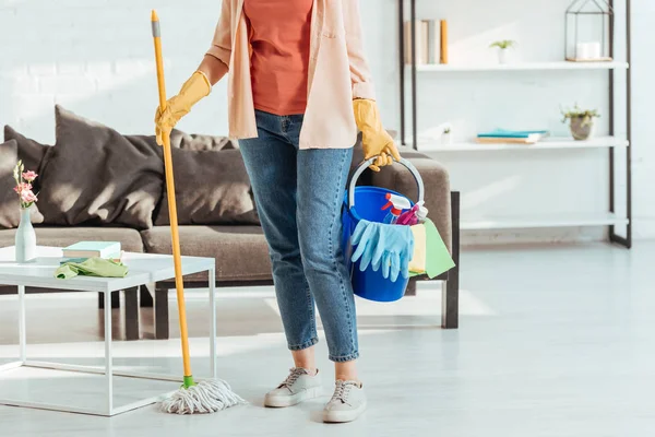 Ausgeschnittene Ansicht einer Frau in Gummihandschuhen, die Mopp und Eimer mit Putzmitteln in der Hand hält — Stockfoto