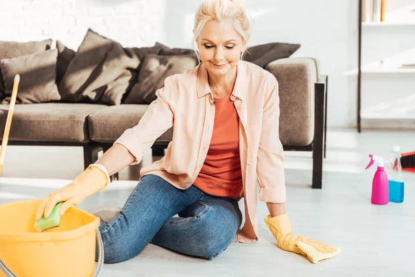 Mujer mayor en guantes amarillos limpiando piso con esponja - foto de stock