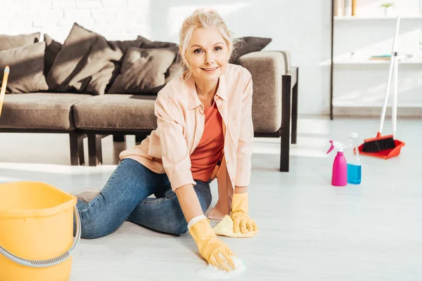 Mulher sênior em luvas de borracha chão de limpeza com pano — Fotografia de Stock