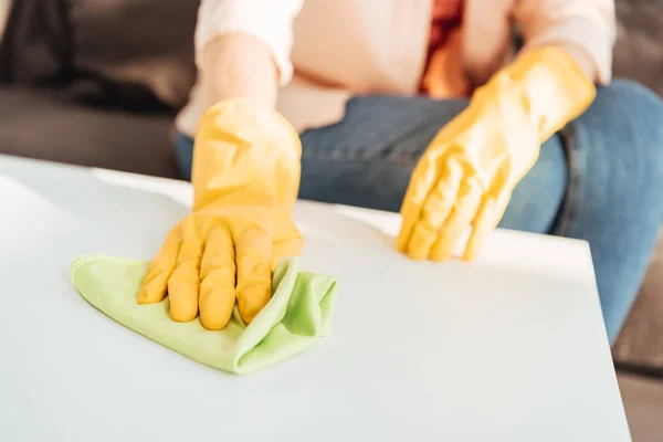 Vista recortada de la mujer en guantes amarillos mesa de limpieza con trapo - foto de stock