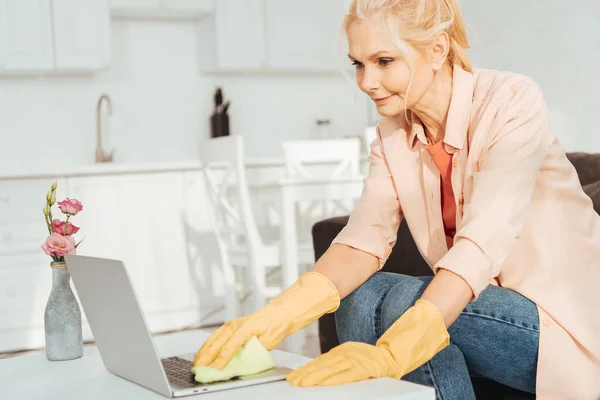 Mujer mayor en guantes de goma limpieza teclado portátil - foto de stock