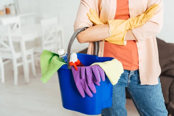Vue recadrée de la femme dans des gants en caoutchouc tenant seau avec des fournitures de nettoyage — Photo de stock