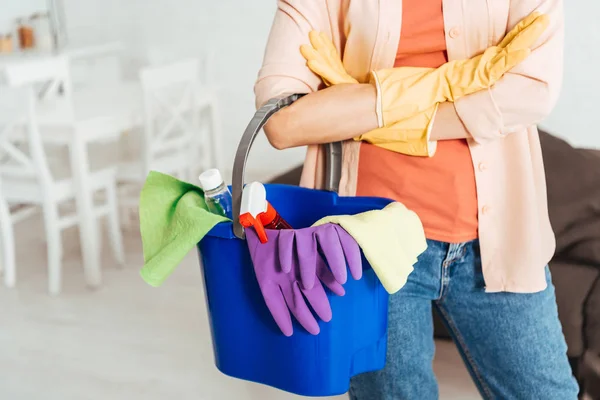 Vista recortada de la mujer en guantes de goma que sostiene el cubo con suministros de limpieza - foto de stock