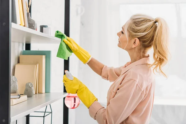 Senior woman with pony tail cleaning shelves with rag — Stock Photo