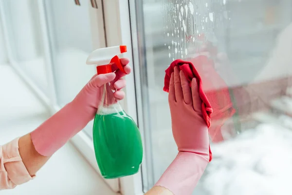 Partial view of woman in pink gloves cleaning window with spray and rag — Stock Photo