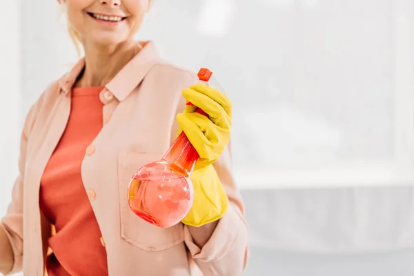Vue recadrée de la femme souriante en gant jaune tenant le flacon pulvérisateur — Photo de stock