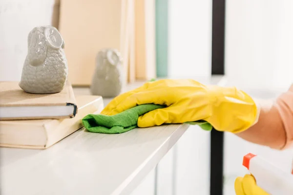 Cropped view of woman in yellow rubber glove cleaning book shelf — Stock Photo