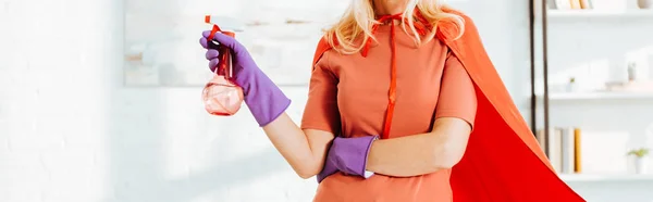 Cropped view of woman in superhero cloak and rubber gloves holding spray bottle — Stock Photo