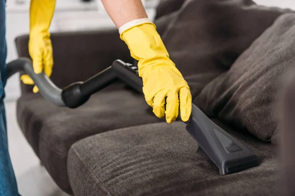 Cropped view of woman in rubber gloves cleaning sofa with vacuum cleaner — Stock Photo