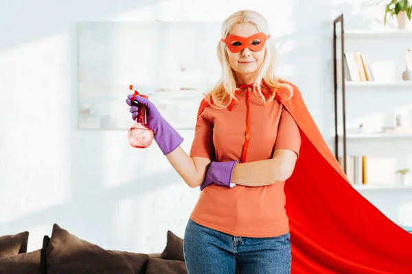 Mulher sênior confiante em traje de super-herói e luvas de borracha segurando frasco de spray — Fotografia de Stock