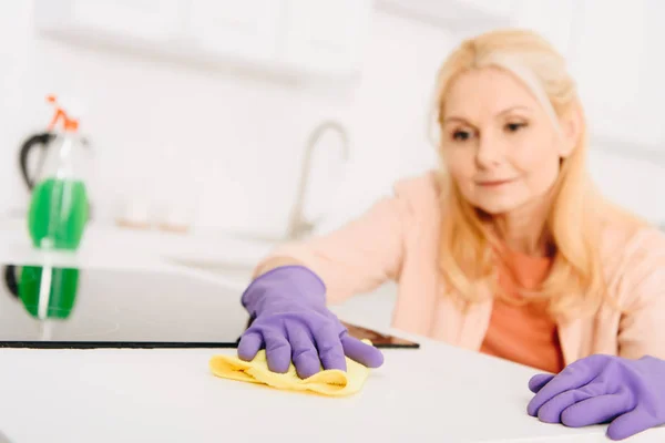 Blonde senior woman cleaning kitchen stove with rag — Stock Photo