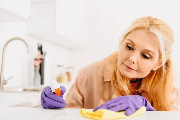 Mulher sênior em luvas roxas limpeza cozinha fogão — Fotografia de Stock