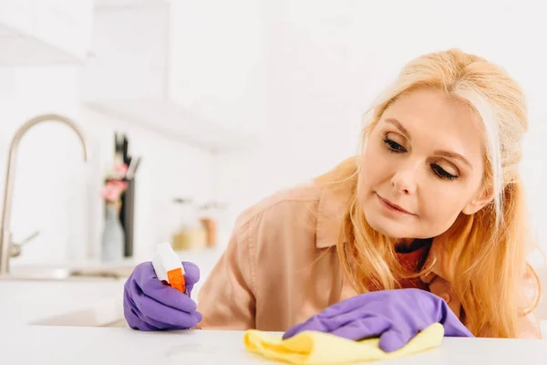 Mujer mayor en guantes morados limpieza cocina estufa - foto de stock