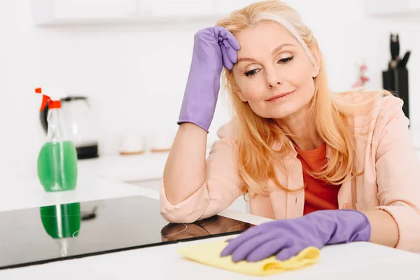 Tired senior woman in rubber gloves cleaning kitchen — Stock Photo