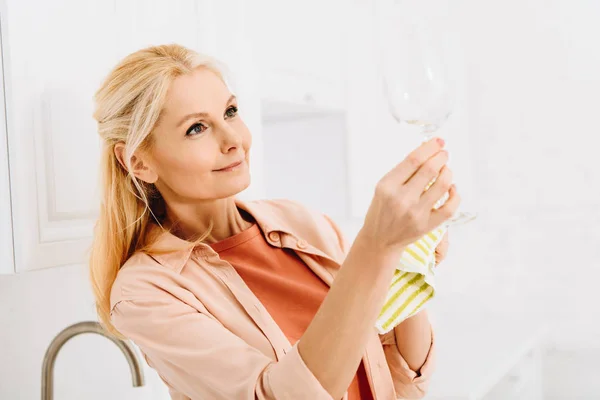 Pleased senior woman wiping wineglass with dishcloth — Stock Photo