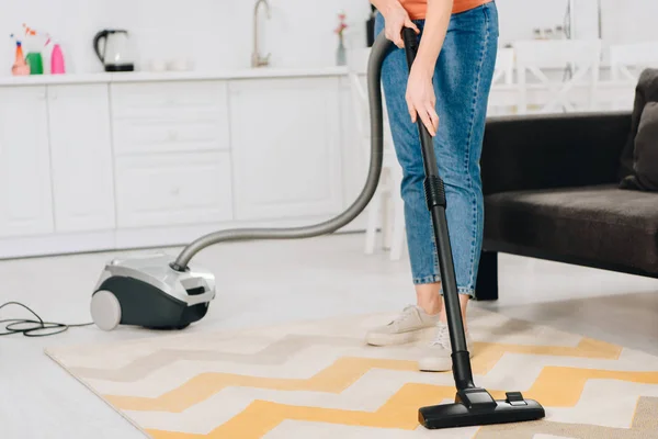 Ausgeschnittene Ansicht einer Frau in Jeans, die Teppich mit Staubsauger putzt — Stockfoto
