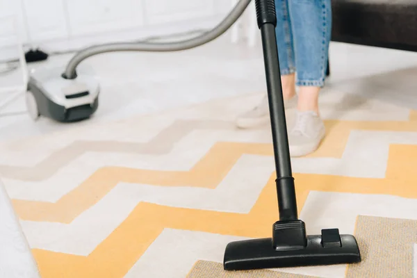 Partial view of woman cleaning striped carpet with vacuum cleaner — Stock Photo