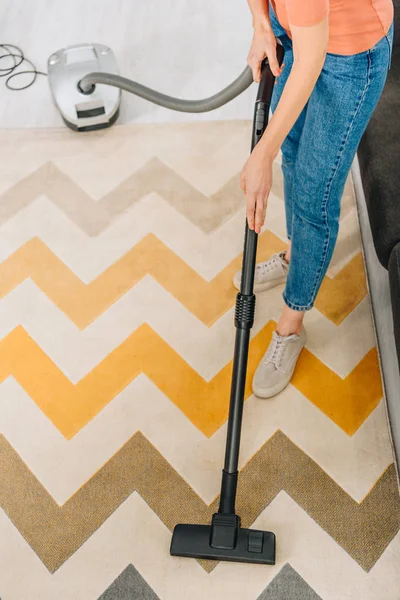 Ausgeschnittene Ansicht einer Frau in Jeans, die Teppich mit Staubsauger putzt — Stockfoto