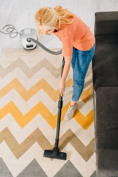 Frau in Jeans putzt Teppich mit Staubsauger — Stockfoto