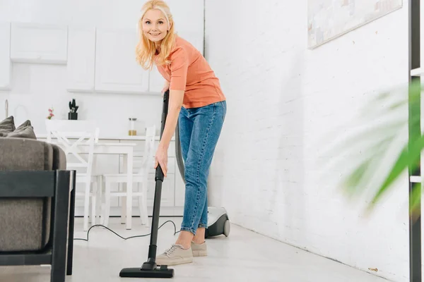 Enthousiaste femme senior nettoyage sol avec aspirateur — Photo de stock