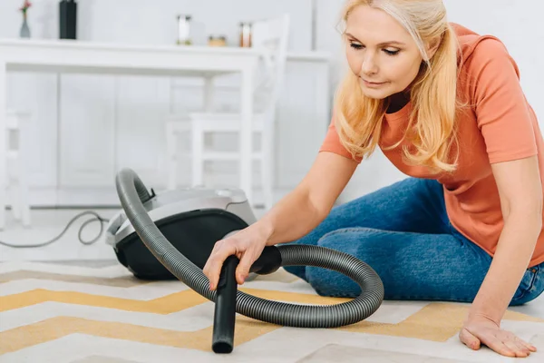 Concentrated blonde woman in jeans using vacuum cleaner — Stock Photo