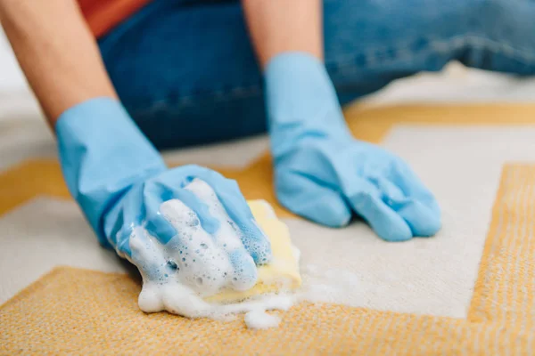 Partial view of woman in rubber gloves cleaning striped carpet with foamy sponge — Stock Photo