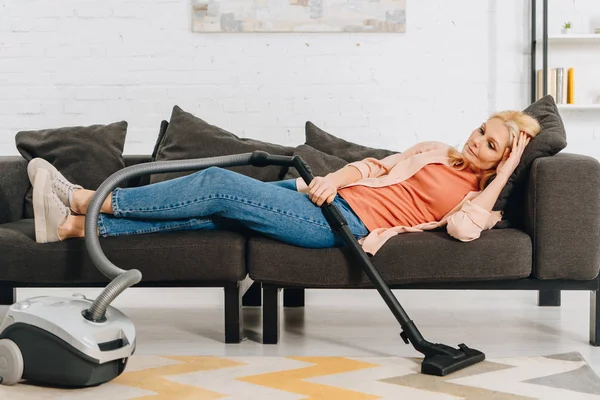 Tired senior woman with vacuum claner lying on sofa — Stock Photo