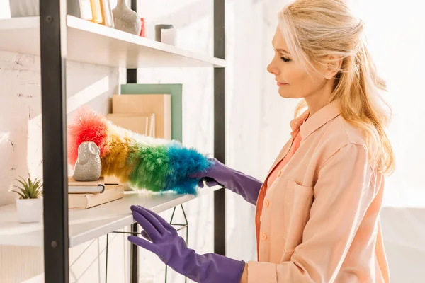 Femme âgée en gants de caoutchouc nettoyage étagères avec chiffon — Photo de stock