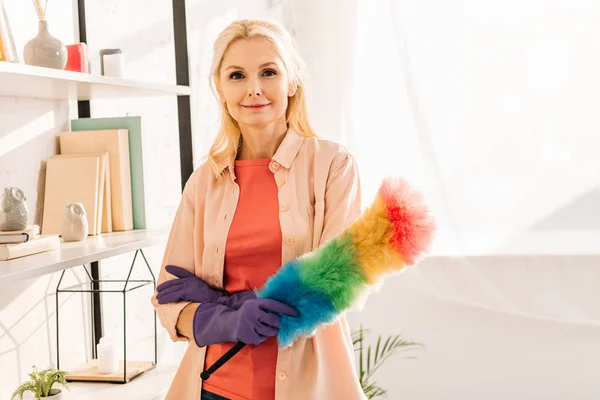 Smiling senior woman in rubber gloves holding bright duster — Stock Photo