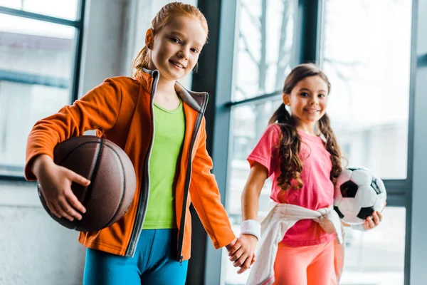 Lindos niños con pelotas cogidas de la mano en el gimnasio - foto de stock