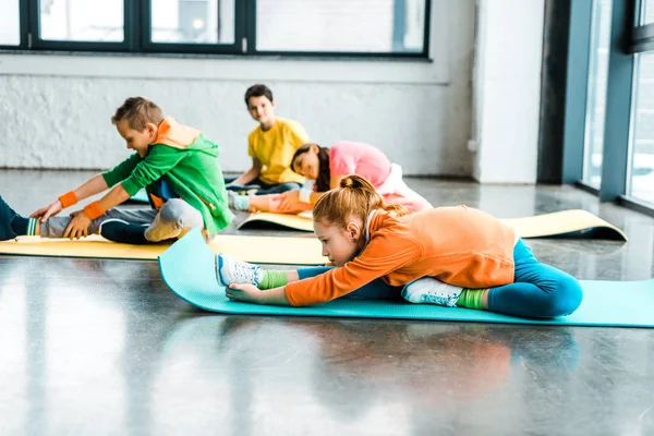 Grupo de niños estirándose sobre coloridas alfombras de fitness - foto de stock