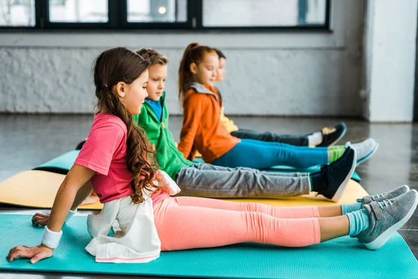 Preteen kids sitting on fitness mats and doing exercise — Stock Photo