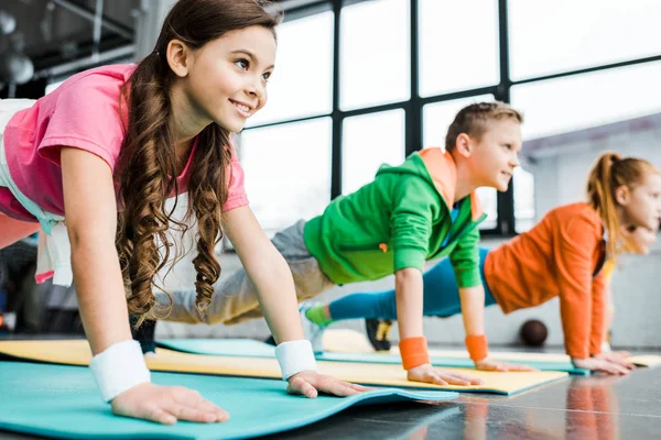 Crianças sorridentes fazendo exercícios de prancha em tapetes de fitness — Fotografia de Stock