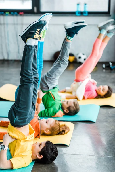 Crianças fazendo exercício castiçal em esteiras no ginásio — Fotografia de Stock