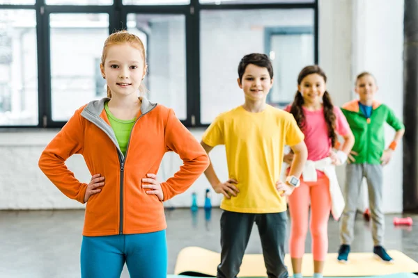 Grupo de niños de pie en el gimnasio con los brazos akimbo - foto de stock