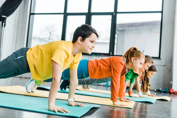 Niños preadolescentes haciendo ejercicio de tablón juntos en el gimnasio - foto de stock