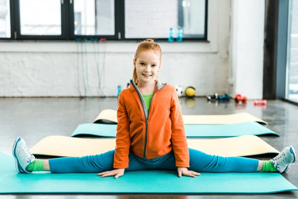 Cute kid doing twine on blue mat in gym — Stock Photo