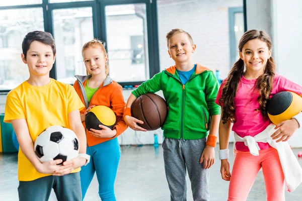 Unbekümmerte Kinder posieren mit Bällen in Turnhalle — Stockfoto