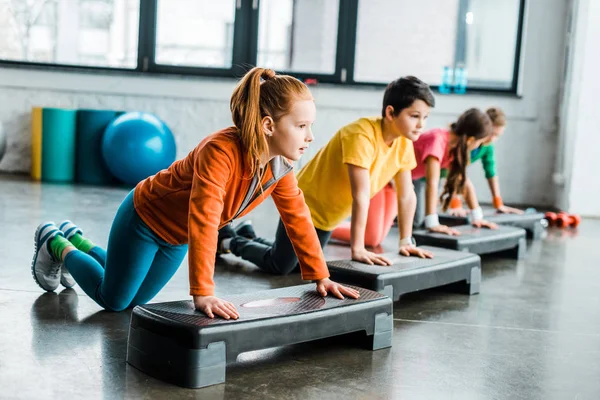 Niños que usan plataformas escalonadas mientras hacen ejercicio push-up - foto de stock