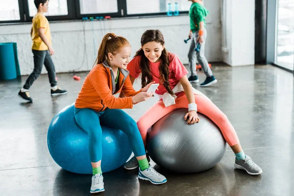Enfants utilisant un smartphone assis sur des balles de fitness — Photo de stock