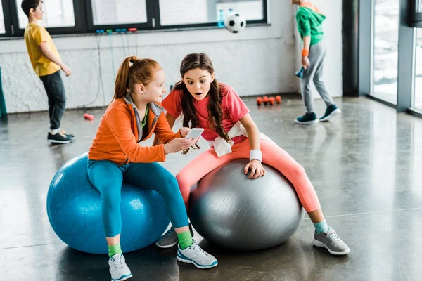 Niños asombrados con smartphone sentado en pelotas de fitness - foto de stock