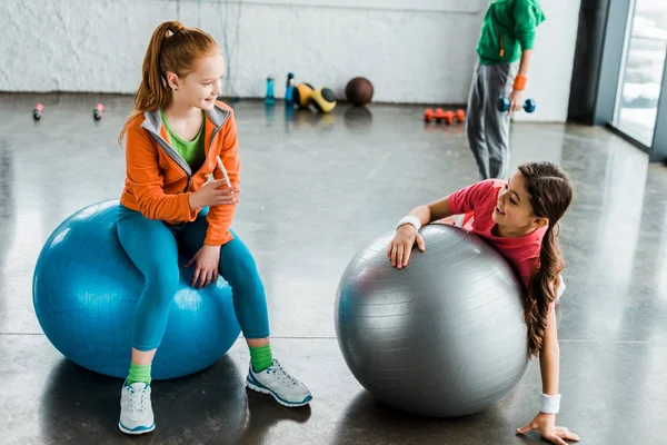 Niños con smartphone usando pelotas de fitness en el gimnasio - foto de stock